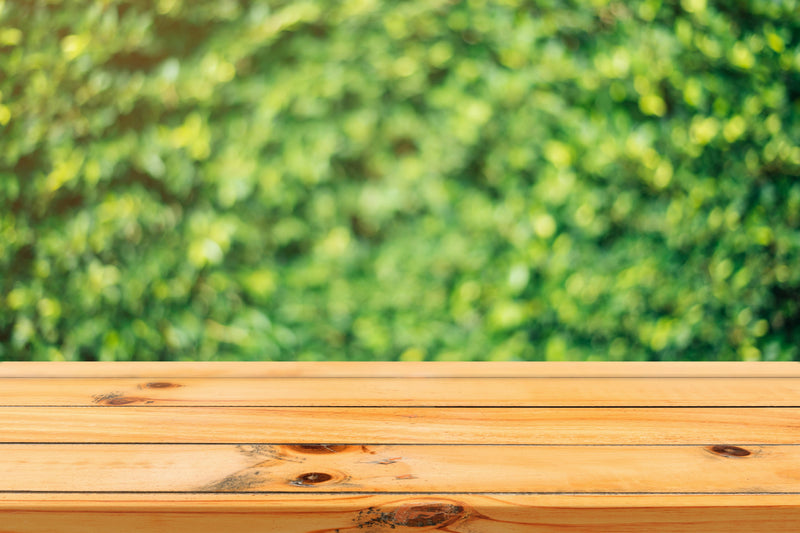 Close-up of a light natural wood tabletop surface with green garden bokeh background