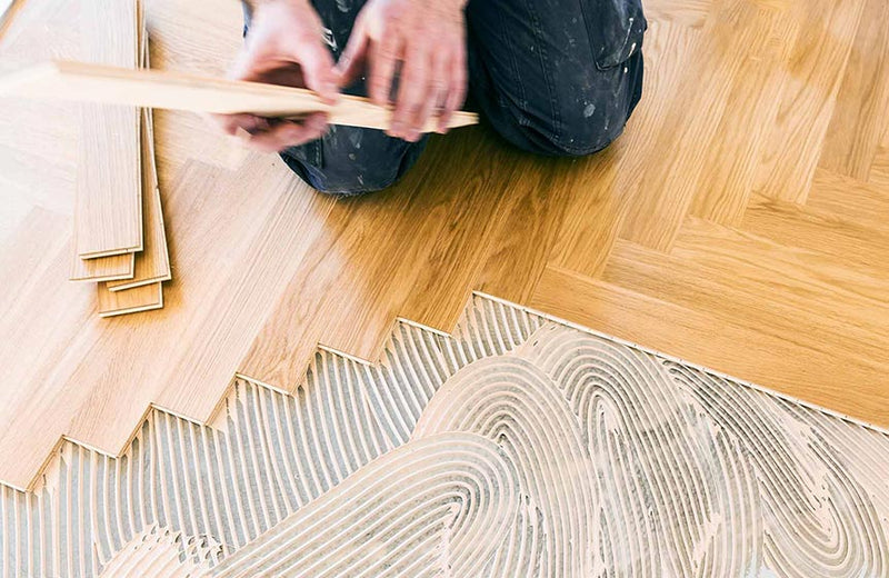 Craftsman gluing engineered herringbone hardwood planks in a zigzag pattern on adhesive bed